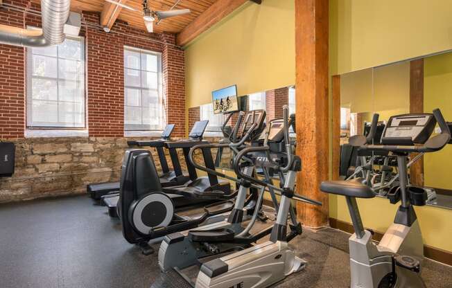 a gym with cardio equipment and weights in a building with brick walls