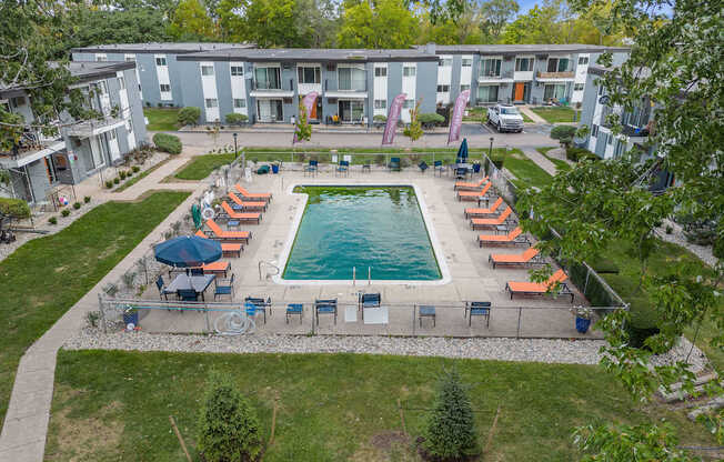 A swimming pool surrounded by chairs and umbrellas in a grassy area.