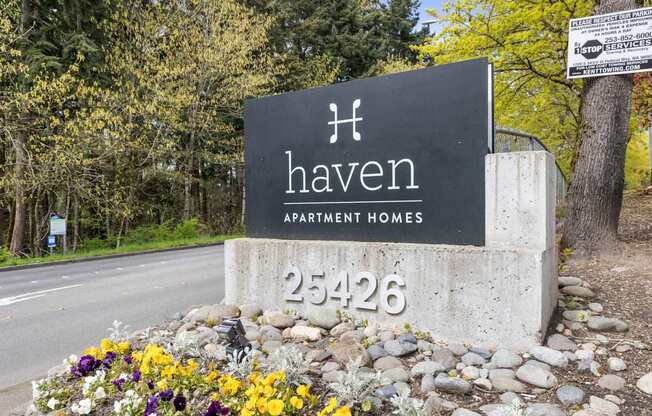 A sign for Haven Apartment Homes is surrounded by flowers and rocks.