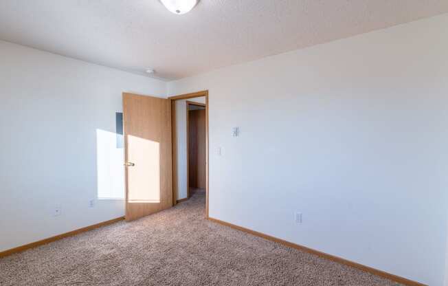 a bedroom with white walls and carpet.  Fargo, ND Sunwood Apartments  | Living and kitchen Fargo, ND Sunwood Apartments