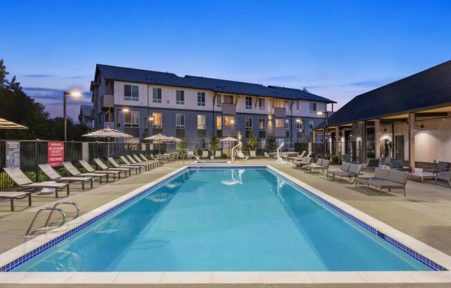 A large swimming pool in front of a building with lounge chairs around it.
