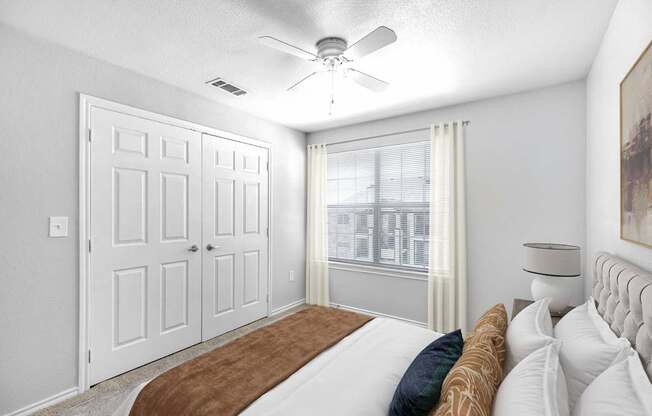 A bedroom with a bed, a ceiling fan, and a window with curtains.