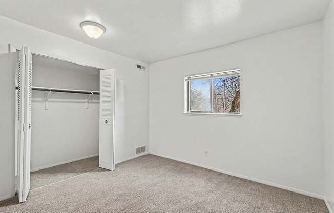 A white bedroom with a window and a white closet at Trappers Cove Apartments, Lansing