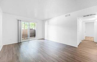 A room with wooden floors and white walls, featuring a sliding glass door.