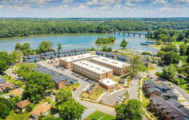 A large building complex is situated in front of a body of water with a bridge in the background.