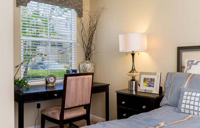 A bedroom with a bed, desk, chair, and window.