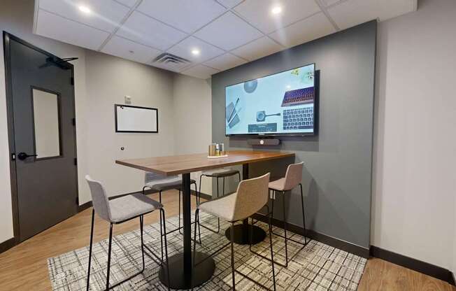 A conference room with a table, chairs, and a screen displaying a presentation.