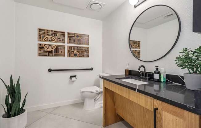 A bathroom with a toilet, sink, mirror, and artwork on the wall.