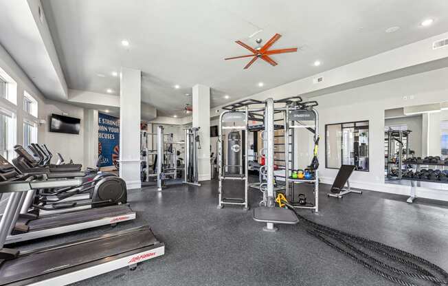 a gym with weights and cardio machines and a ceiling fan