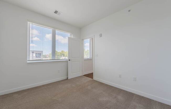 A room with a carpeted floor and two windows.