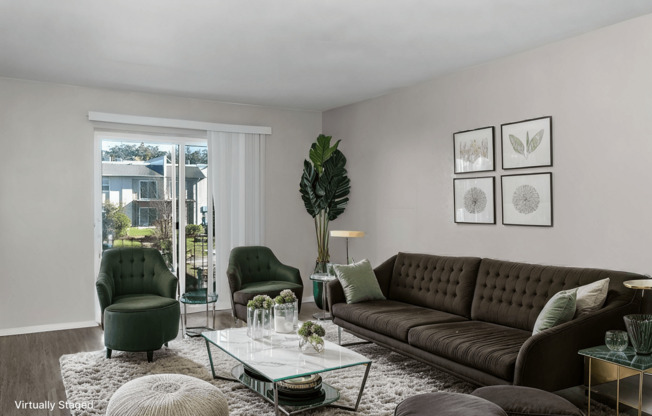A living room with a brown couch, green armchairs, and a glass coffee table.