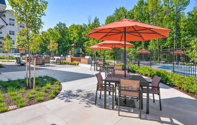 a patio with tables and umbrellas next to a swimming pool
