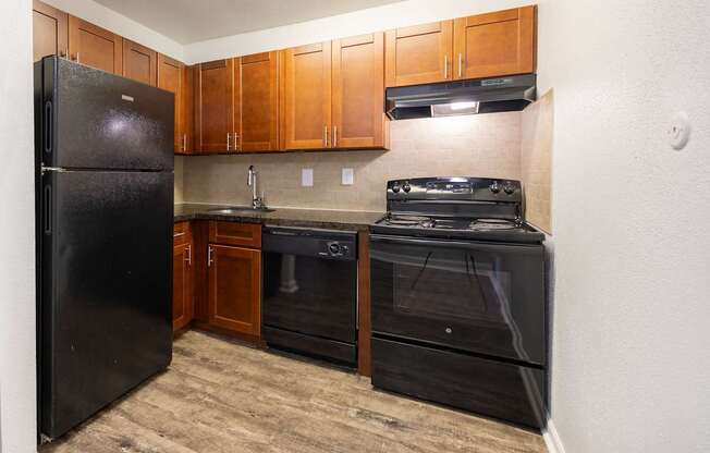 A black refrigerator is in a kitchen with wooden cabinets.