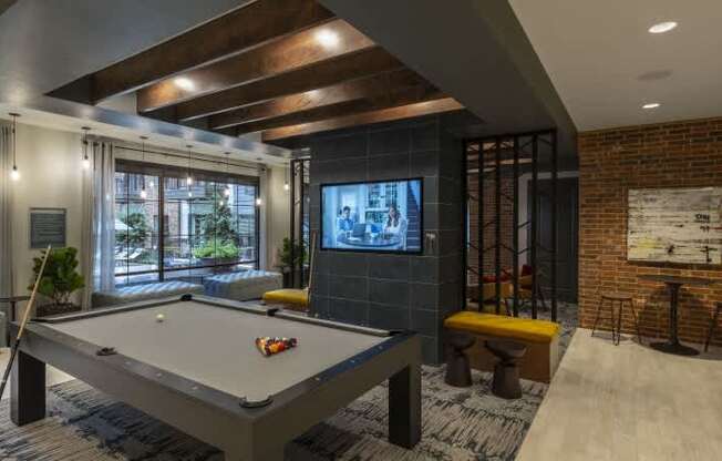 A pool table is in the middle of a room with a brick wall and a television.
