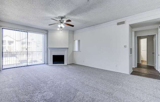A large living room at Saxony at Chase Oaks Apartments in Dallas, TX, featuring built-in shelving above the fireplace, a ceiling fan and carpeted floors.