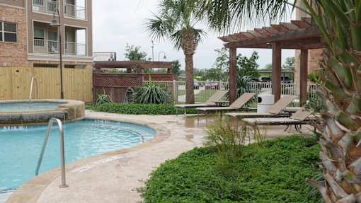 A pool surrounded by a concrete patio and a wooden pergola.
