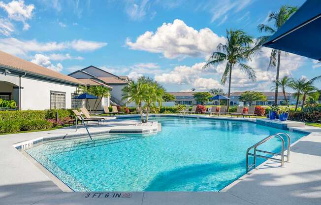 A large outdoor swimming pool with lounge chairs and an adjacent clubhouse overlooking a body of water