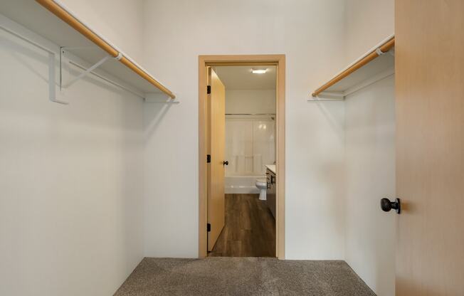A walk-in closet with custom shelving, taupe carpets, white walls and access to the bathroom.at Shoreline Village, Richland, 99352