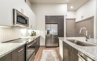 A kitchen with a refrigerator, microwave, and sink.at The Bridge at McKinney, McKinney