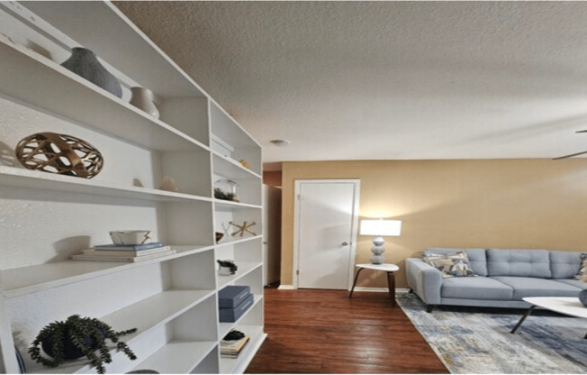 A living room with a grey couch and a white shelf with various objects on it.