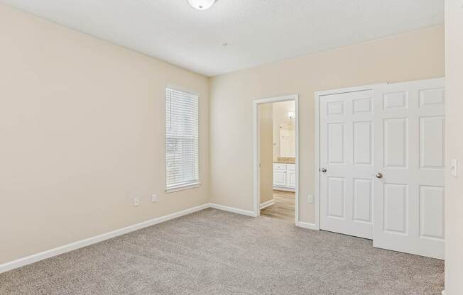 A room with a white door, carpeted floor, and a window with blinds.