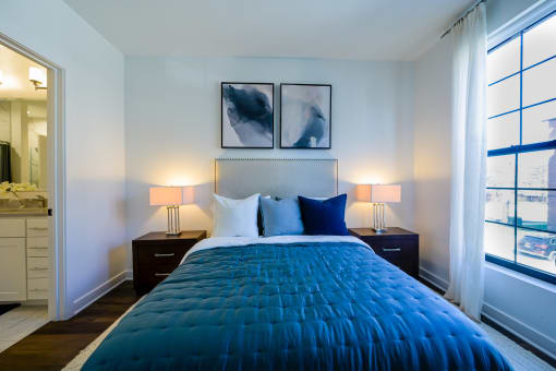 a bedroom with a blue comforter on a bed and two windows