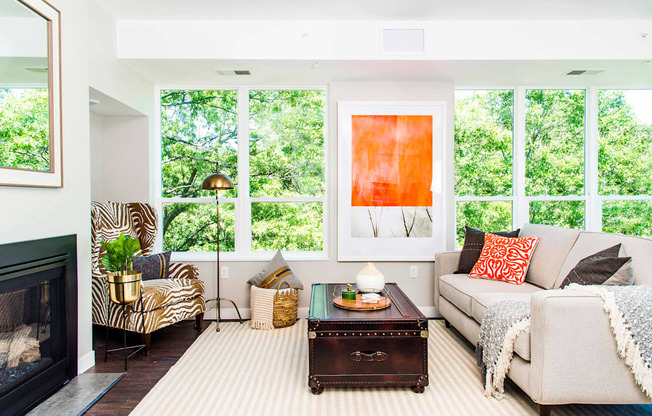An elegant living room with luxurious stain-resistant plank flooring, a gas fireplace, and expansive windows that offer picturesque views of nature. A seamless transition to a balcony creates a spacious indoor-outdoor connection.