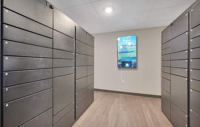A hallway with a row of lockers on the left and a TV screen on the right.