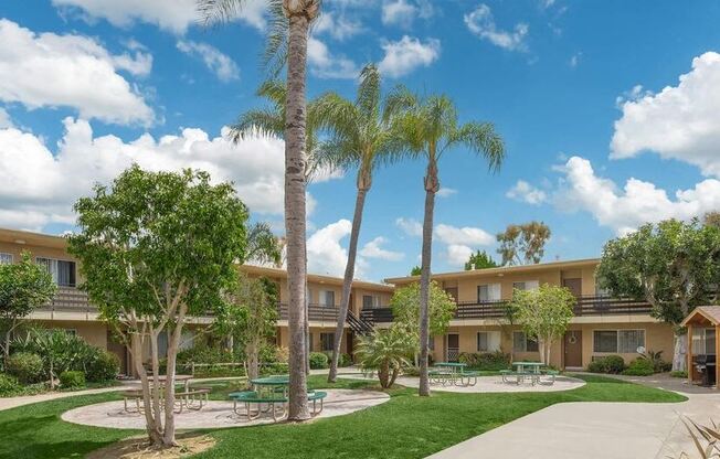 a courtyard with palm trees in front of a building at Villa La Paz Apartments, California, 90706