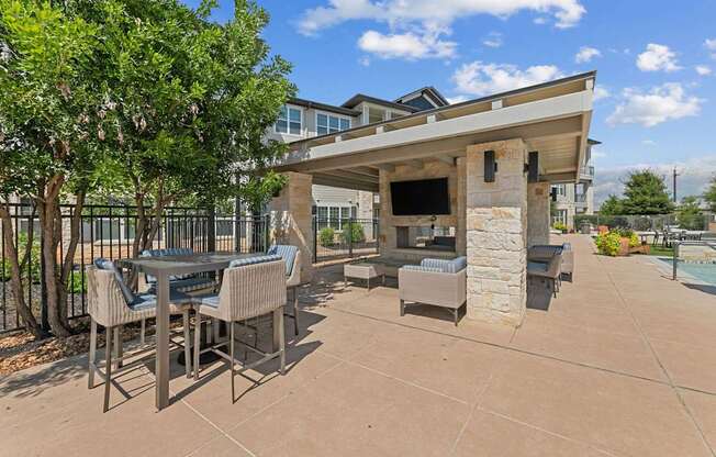 A patio with a table and chairs is surrounded by a pool and a building.