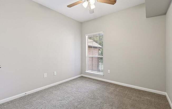 A room with a ceiling fan and a window with blinds.