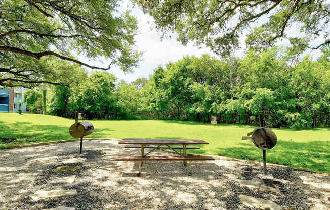 A picnic table is set up in a gravel area with trees in the background.
