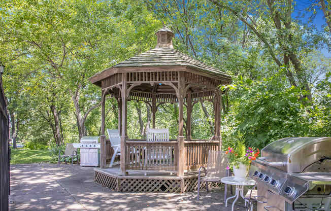 a gazebo in a backyard with trees and a grill