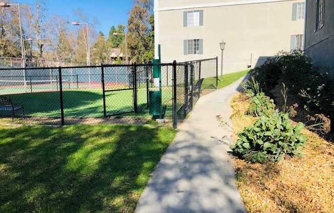 A walkway leads to a building with a tennis court behind a fence.