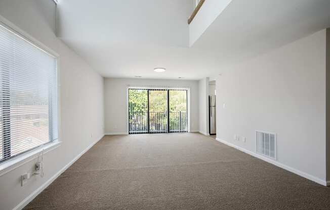 A spacious room with a carpeted floor and a sliding glass door leading to a balcony.
