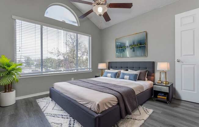 A bedroom with a large bed, a ceiling fan, and a painting on the wall.