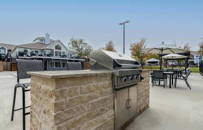 a patio with a grill and tables with chairs and umbrellas