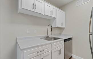 an empty kitchen with white cabinets and a sink and refrigerator