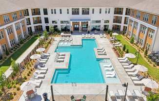 A large swimming pool surrounded by lounge chairs and umbrellas in a courtyard.