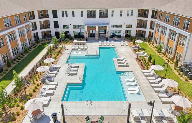 A large swimming pool surrounded by lounge chairs and umbrellas in a courtyard.