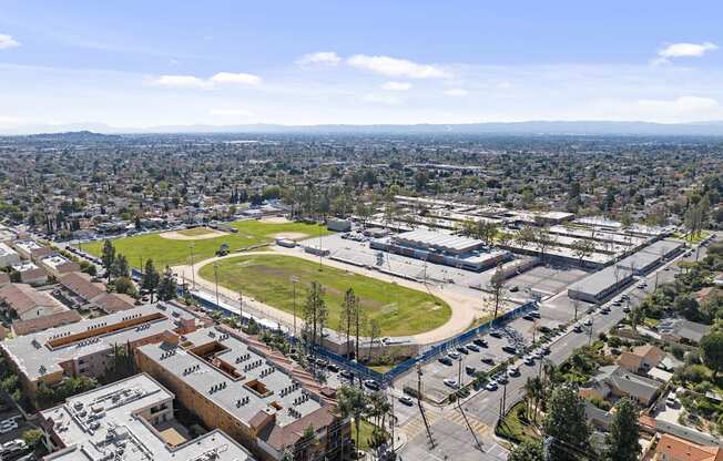 A view of a city from a high vantage point with buildings, a parking lot, and a green field.