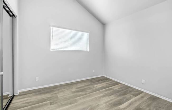 a bedroom with white walls and wood flooring and a window