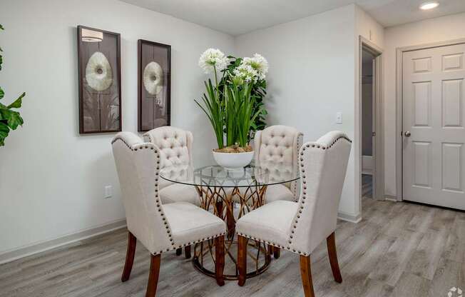 A dining room with a glass table and white chairs.