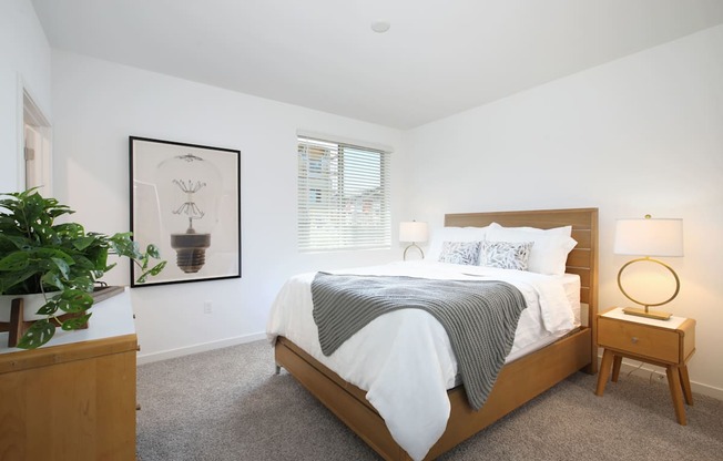 A bedroom with a bed, nightstand, and a potted plant.