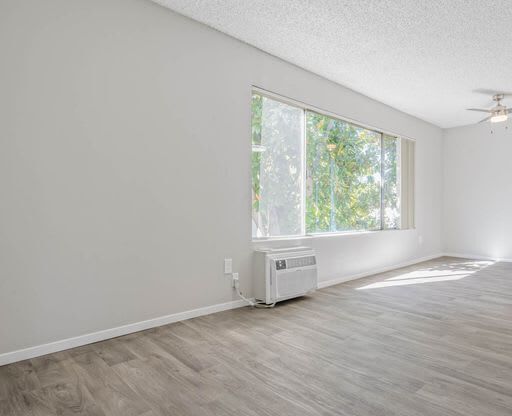 an empty living room with a large window and wooden floors at The Arches Apartments, El Cajon, 92021