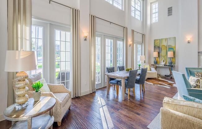 Resident clubhouse with high windows, wood flooring, high ceiling, and several chairs and tables at Evergreens at Mahan apartments  in Tallahassee, FL