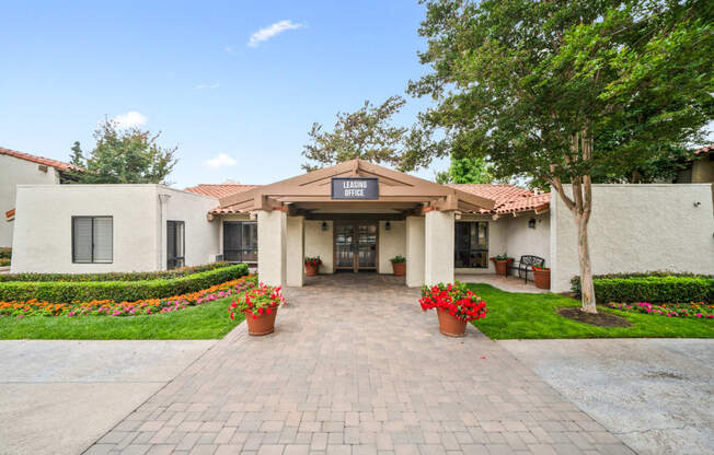 the view of the front entrance of a white building with potted plants and trees