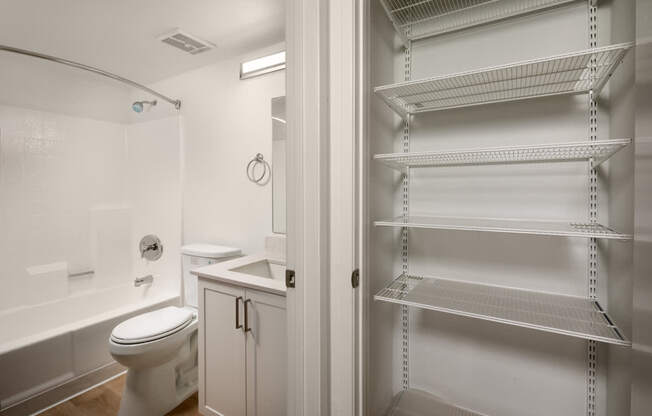 A white bathroom with a toilet, sink, and shelving unit.