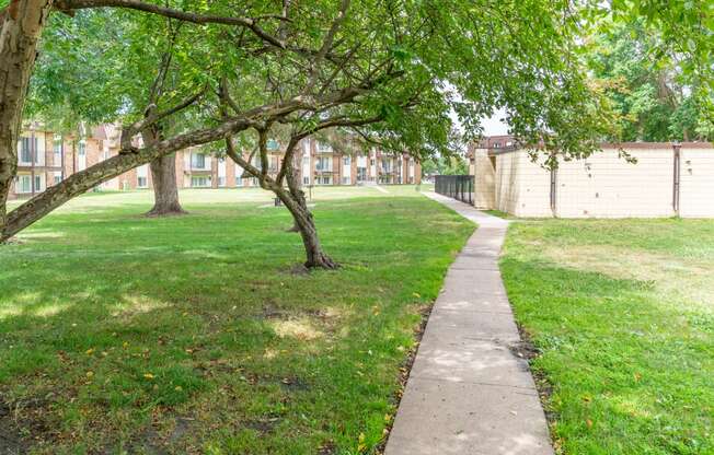 a grassy area with trees and a concrete path in front of a building
