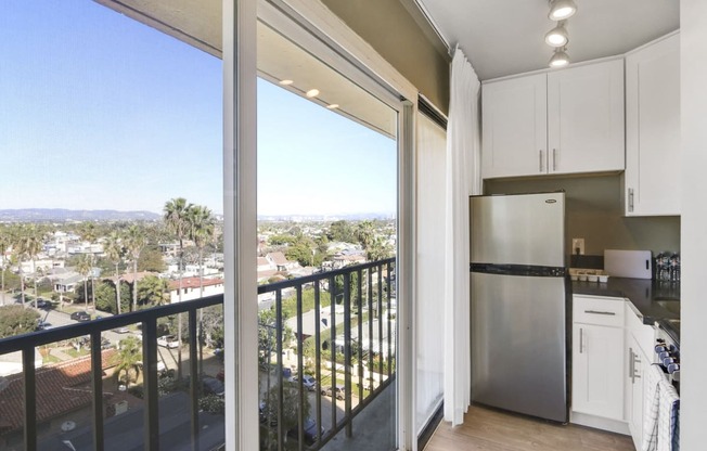 Studio Kitchen with Stainless Steel Appliances including two door refrigerator, gray quartz countertops, white kitchen cabinets, large windows